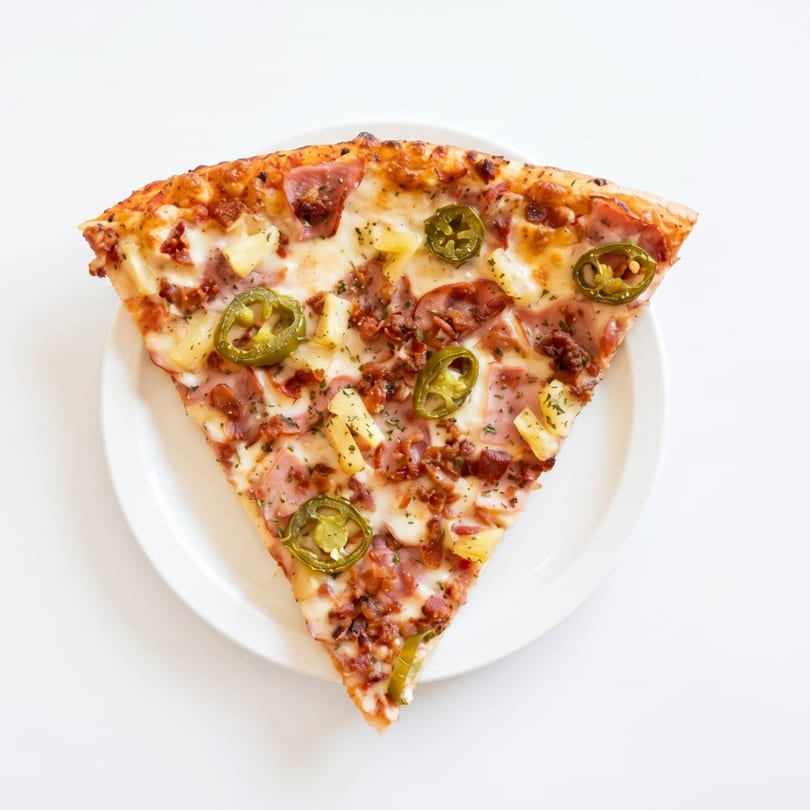 A single slice of pizza with pineapple, ham, bacon, and jalapeños on a white plate.